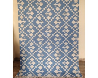 Puede incluir: Una alfombra azul y blanca con un diseño geométrico. La alfombra tiene un borde de flecos.
