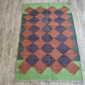 K&ouml;nnte beinhalten: Ein gewebter Teppich mit einem karierten Muster in Braun-, Gr&uuml;n- und Oranget&ouml;nen. Der Teppich hat ein Rautenmuster mit abwechselnden Farben.