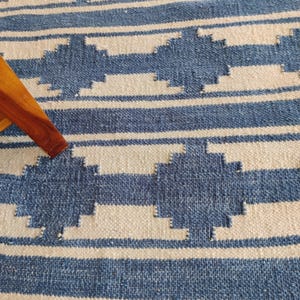 Könnte beinhalten: Ein blauer und weißer Teppich mit geometrischem Muster. Der Teppich ist aus gewebtem Stoff und hat eine weiche Textur.