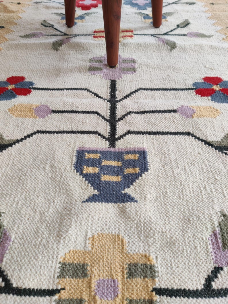 handwoven wool rug features a floral tribal kilim design with soft beige, red, blue, and pastel tones. Made from premium natural wool, this flatweave rug is durable, eco-friendly, and perfect for living rooms, bedrooms, or boho home décor. Each rug is handcrafted by skilled artisans, making it a unique and timeless piece for modern and traditional interiors.