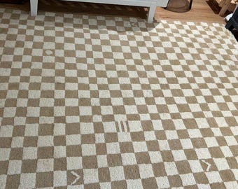 May include: A beige and white checkered rug with a geometric pattern. The rug has a subtle texture and is made of a soft material.