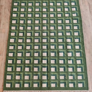 Puede incluir: Una alfombra geom&eacute;trica con estampado verde y blanco con borde de flecos. La alfombra tiene un patr&oacute;n de cuadros con cuadrados de diferentes tonos de verde y blanco.