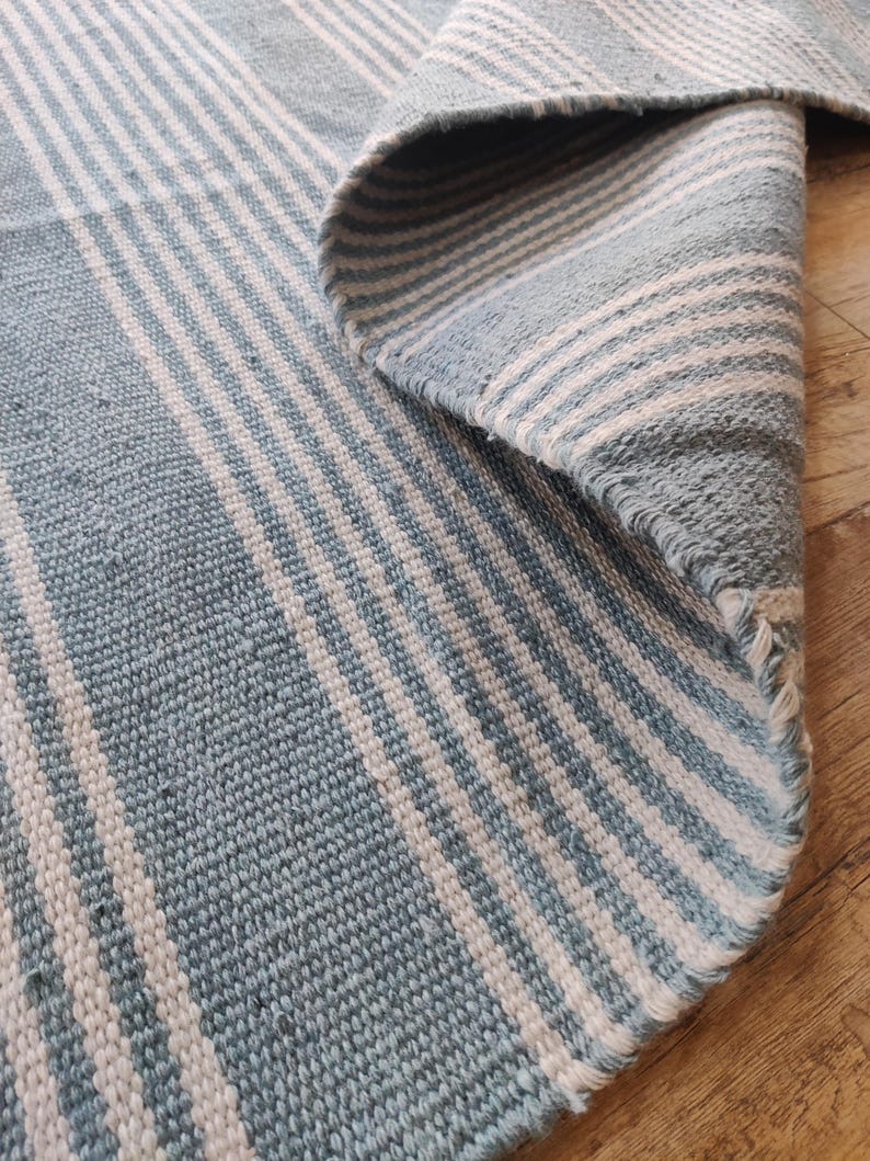 Pu&ograve; includere: Un tappeto a righe blu e bianche con un bordo arrotolato. Il tappeto presenta una trama tessuta e un motivo a righe blu e bianche alternate. Il tappeto &egrave; realizzato in un materiale morbido ed &egrave; adatto per uso interno.