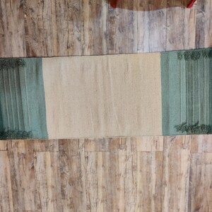 May include: A long, rectangular rug with a beige center and green stripes on either end. The rug has a fringed edge.