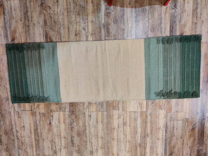 May include: A long, rectangular rug with a beige center and green stripes on either end. The rug has a fringed edge.