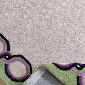 Hand tufted wool rug with green border and purple chain pattern on neutral background, modern designer area rug for living room or bedroom