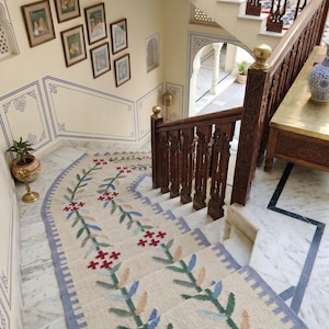 Puede incluir: Una escalera con una alfombra de corredor color crema con un diseño floral en verde, azul y rojo. Las escaleras tienen una barandilla de madera y están rodeadas de paredes color crema con obras de arte enmarcadas.