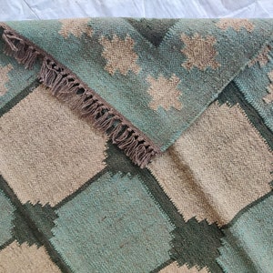 May include: A woven rug with a geometric pattern in shades of green, brown, and beige. The rug has a fringe border.
