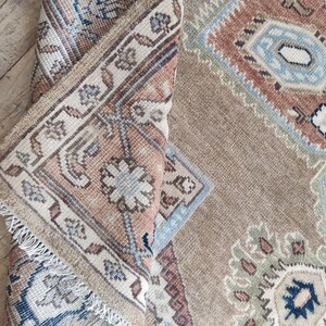 May include: A close-up of a beige and brown rug with a traditional Persian design. The rug has a fringe border and intricate patterns in shades of blue, green, and red.