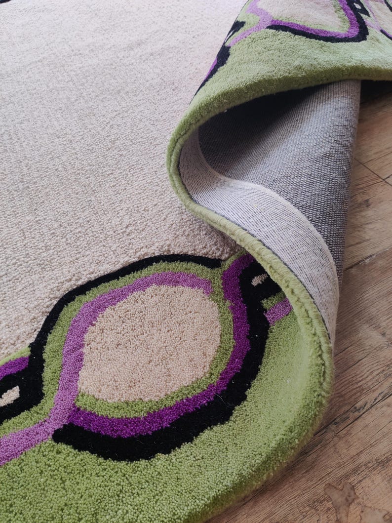 May include: A rolled-up area rug with a beige background and a green, black, and purple circular design. The rug's edge is green, and the design is visible on the rolled-up portion.