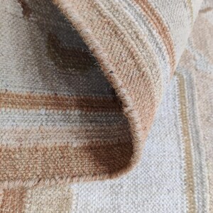 May include: Close-up of a beige and brown striped rug with a fringe edge. The rug has a subtle pattern of stripes and a soft, textured feel.