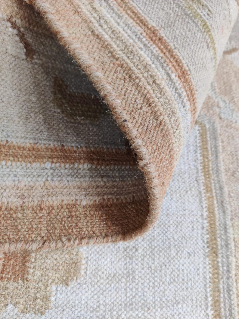 May include: Close-up of a beige and brown striped rug with a fringe edge. The rug has a subtle pattern of stripes and a soft, textured feel.