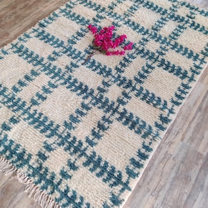 May include: A white and teal blue rug with a geometric pattern. The rug has a fringe border and is made of a soft, fluffy material.