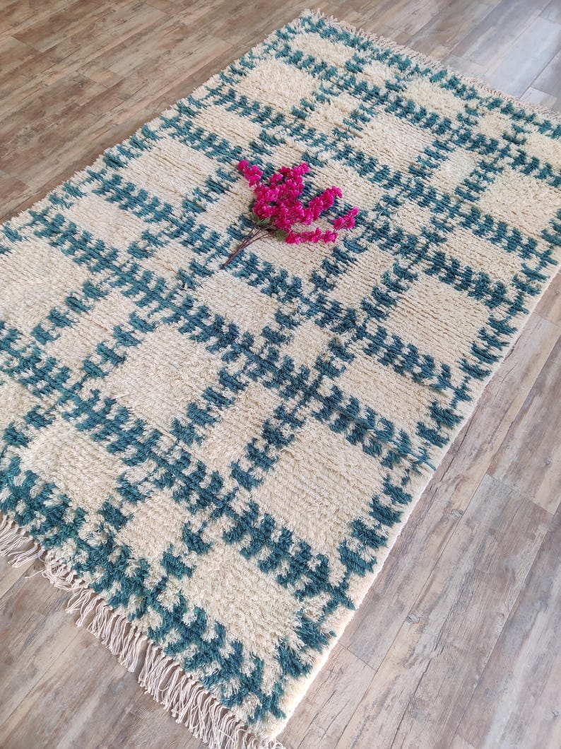 May include: A white and teal blue rug with a geometric pattern. The rug has a fringe border and is made of a soft, fluffy material.