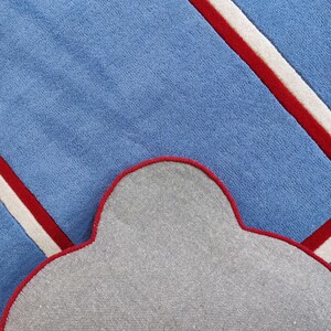 May include: A blue rug with a cloud-shaped design. The rug features diagonal stripes in red and white against a light blue background. The underside of the rug is gray with a red border.