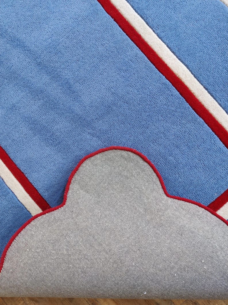 May include: A blue rug with a cloud-shaped design. The rug features diagonal stripes in red and white against a light blue background. The underside of the rug is gray with a red border.