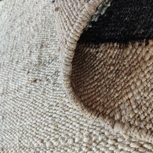 K&ouml;nnte beinhalten: Nahaufnahme eines Naturfaser-Teppichs mit gewebter Textur. Der Teppich hat eine hellbraune Farbe mit schwarzen Streifen.