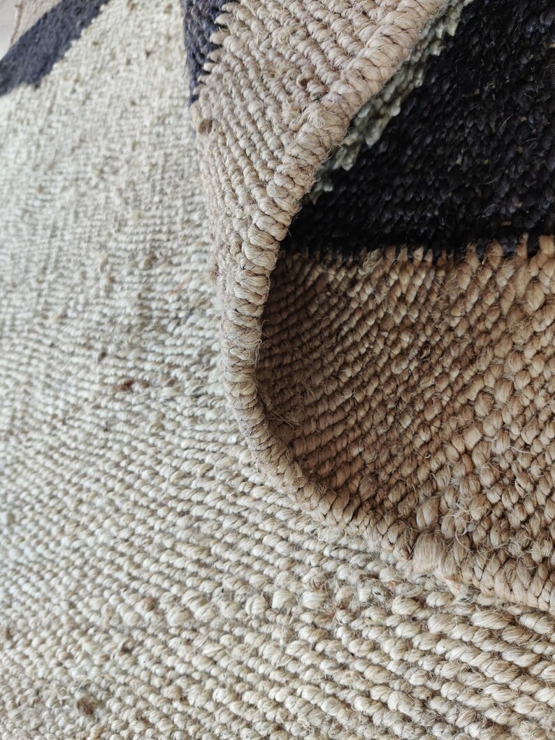 K&ouml;nnte beinhalten: Nahaufnahme eines Naturfaser-Teppichs mit gewebter Textur. Der Teppich hat eine hellbraune Farbe mit schwarzen Streifen.