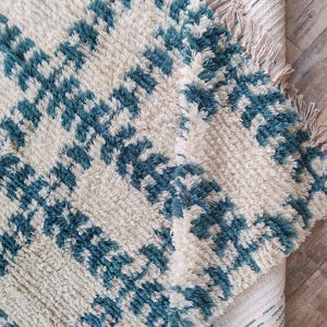May include: A white and blue patterned rug with a fringe border. The rug has a soft, fluffy texture and is made of wool.