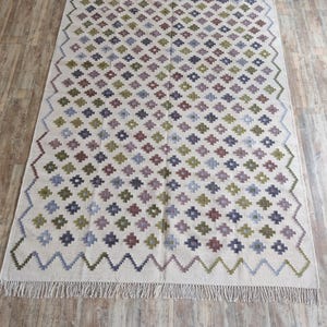 May include: A white rug with a geometric pattern in shades of green, purple, and blue. The rug has a fringe border.