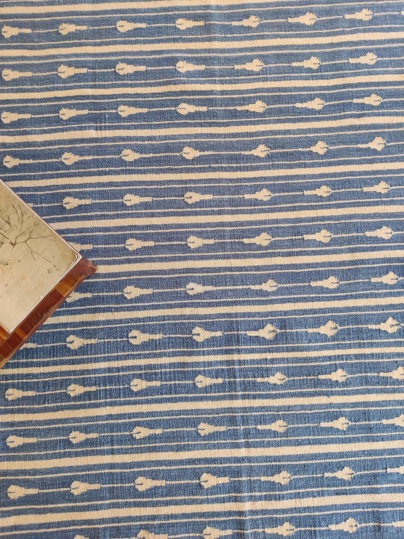 Op de afbeelding: Een blauw en wit gestreept tapijt met een subtiel patroon van witte pijlen. Het tapijt heeft een zachte, textuur en is perfect om elke kamer een vleugje stijl te geven.