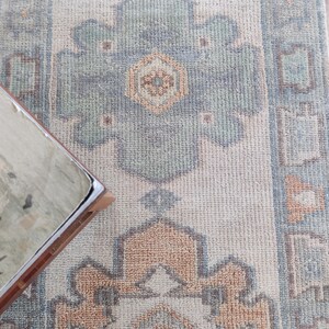May include: A light beige rug with a geometric pattern in shades of blue, green, and pink. The rug has a fringed border.