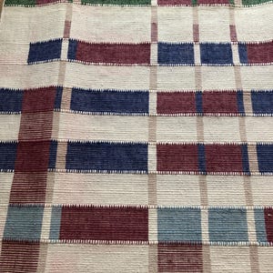 Puede incluir: Una alfombra tejida con un patr&oacute;n de cuadros en tonos de rojo, azul, verde y blanco.