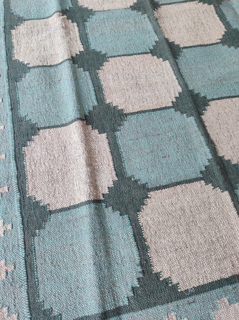 May include: A woven rug with a checkered pattern in shades of teal, gray, and dark green.