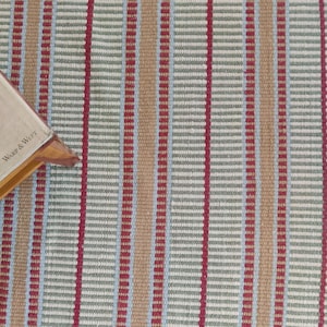 handloom wool blanket showcasing a vibrant striped pattern in red, green, and beige. The wool texture appears soft and inviting, ideal for home decor use. This woolen throw adds a cozy touch to any living room or bedroom, epitomizing luxury textiles with its premium craftsmanship. Known for its durability and softness, this artisan blanket suits all seasons and enhances any space with its elegant desig
