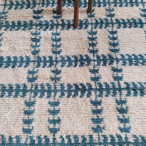 May include: A white and blue patterned rug with a geometric design. The rug has a fluffy texture and is made of wool.