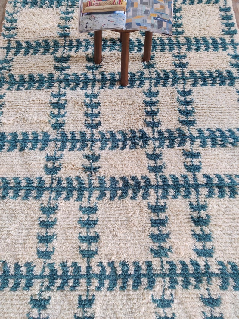 May include: A white and blue patterned rug with a geometric design. The rug has a fluffy texture and is made of wool.