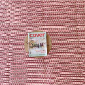 May include: A red and cream-colored patterned rug with a magazine on a wooden coaster. The magazine cover reads "cover" with the text "AWAKEN THE SPIRITS" below a landscape image. The rug's pattern is a repeating geometric design.