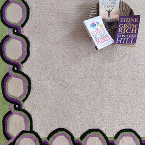 Hand tufted wool rug with green border and purple chain pattern on neutral background, modern designer area rug for living room or bedroom