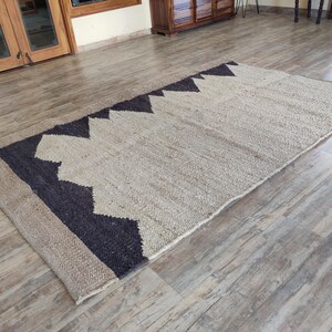K&ouml;nnte beinhalten: Ein Naturfaser-Teppich mit einem geometrischen Muster in Schwarz und Wei&szlig;. Der Teppich ist aus Jute und hat eine gewebte Textur.