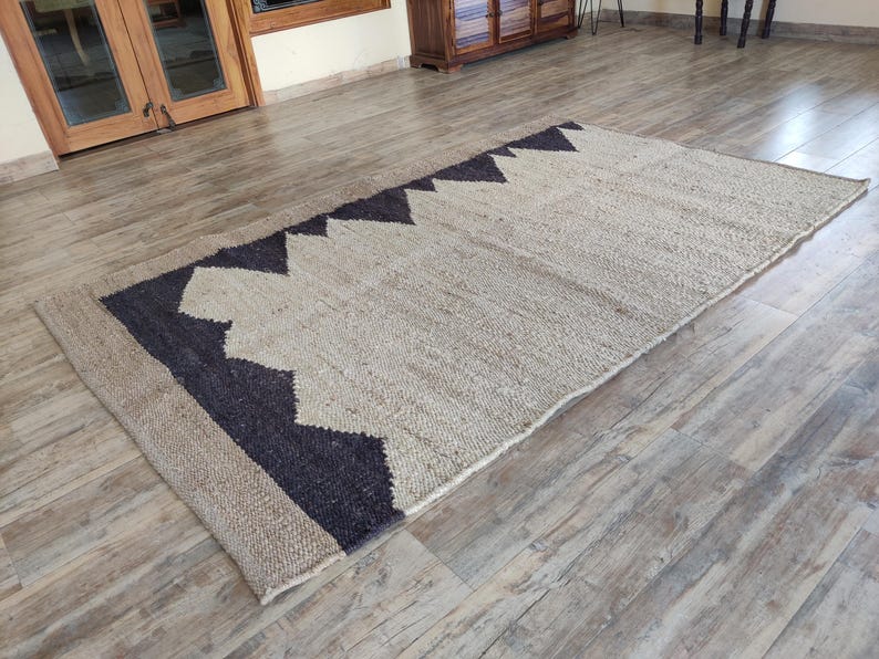 K&ouml;nnte beinhalten: Ein Naturfaser-Teppich mit einem geometrischen Muster in Schwarz und Wei&szlig;. Der Teppich ist aus Jute und hat eine gewebte Textur.