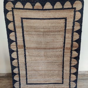 May include: A rectangular jute rug with a black border and a pattern of black teardrop shapes around the edge.