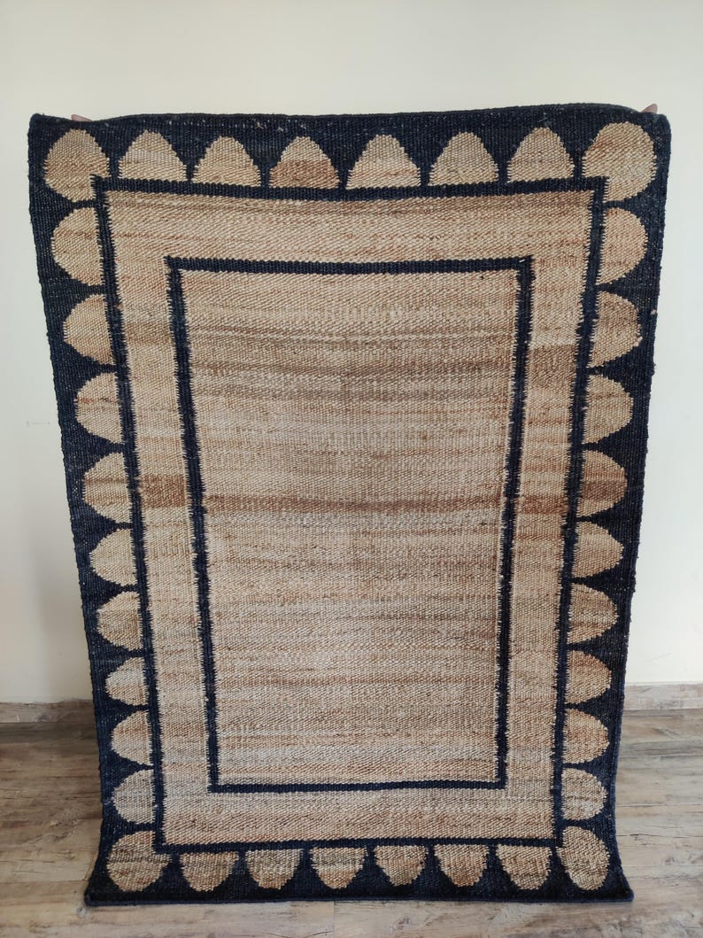 May include: A rectangular jute rug with a black border and a pattern of black teardrop shapes around the edge.