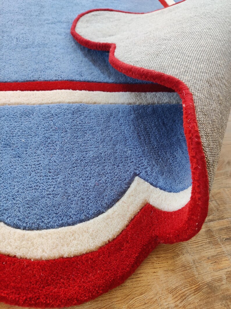 May include: A blue rug with a red and white border. The rug has a soft, textured surface and a decorative design. The rug's dimensions are not visible in the image.