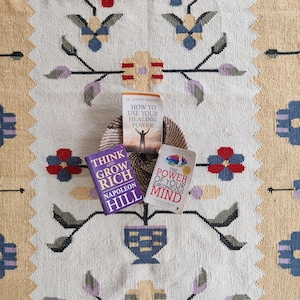 handwoven wool rug features a floral tribal kilim design with soft beige, red, blue, and pastel tones. Made from premium natural wool, this flatweave rug is durable, eco-friendly, and perfect for living rooms, bedrooms, or boho home décor. Each rug is handcrafted by skilled artisans, making it a unique and timeless piece for modern and traditional interiors.