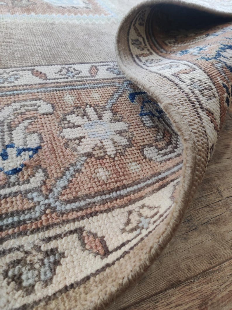 May include: Close-up of the edge of a beige rug with a brown and blue patterned border. The rug has a soft, woven texture.