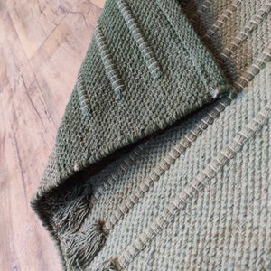 May include: A green woven rug with a textured pattern. The rug has a fringe border.