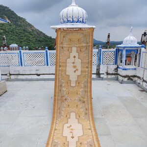 May include: A long, beige runner rug with a traditional floral pattern. The rug is displayed on a rooftop with a blue and white dome in the background.