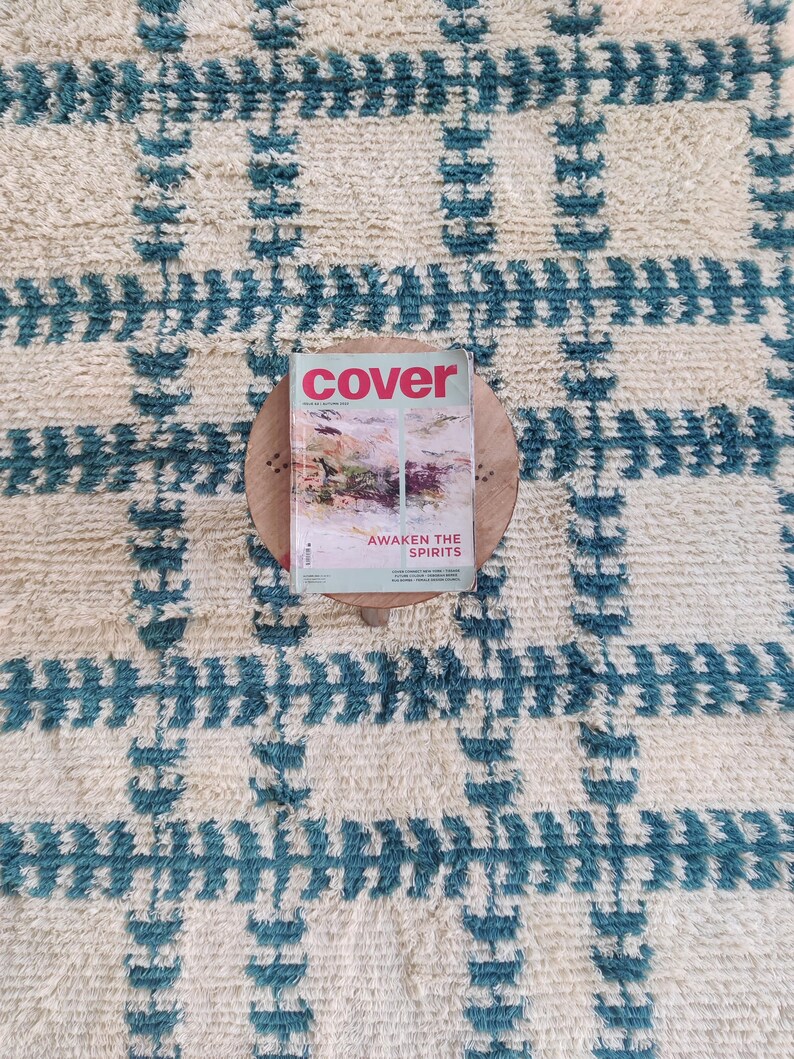 May include: A white and blue patterned rug with a magazine titled "cover" on top of a wooden round stand. The magazine cover features a colorful abstract design and the text "Awaken the Spirits".