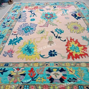 K&ouml;nnte beinhalten: Ein gro&szlig;er, rechteckiger Teppich mit einem hellrosa Mittelfeld und einem t&uuml;rkisfarbenen Rand. Der Teppich weist farbenfrohe Blumenmuster in Blau-, Gelb-, Rot- und Gr&uuml;nt&ouml;nen auf. Der Text "HOUSE OF KILIMS" ist am Rand sichtbar.