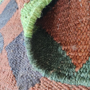 K&ouml;nnte beinhalten: Nahaufnahme eines gewebten Teppichs mit einem karierten Muster in Braun-, Gr&uuml;n- und Graut&ouml;nen. Der Teppich ist aus Naturfasern gefertigt und hat eine raue Textur.