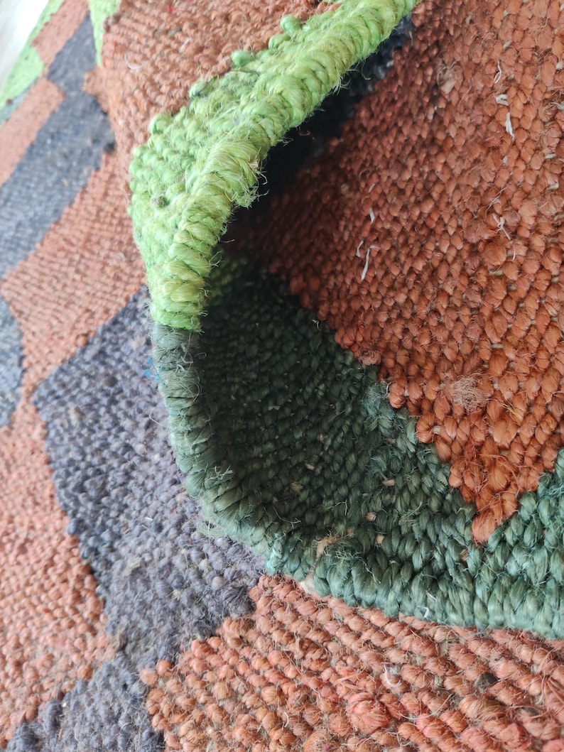K&ouml;nnte beinhalten: Nahaufnahme eines gewebten Teppichs mit einem karierten Muster in Braun-, Gr&uuml;n- und Graut&ouml;nen. Der Teppich ist aus Naturfasern gefertigt und hat eine raue Textur.