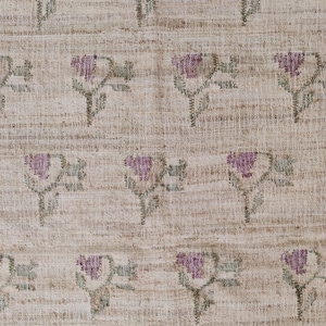 Op de afbeelding: Een close-up van een beige stof met een herhalend patroon van kleine roze bloemen en groene bladeren.