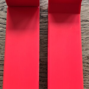 May include: Two red 3D printed plastic parts with a yellow plastic piece on each side. The red parts have a rectangular shape with a circular opening at the top. The yellow pieces have two holes.