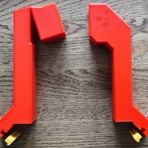 May include: Two red plastic 3D printed corner braces with a yellow plastic piece on the bottom of each brace. The brace on the right has the text "open 3D" printed on it.