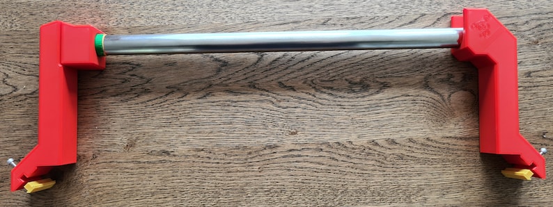 May include: A red metal tool with a silver bar and yellow plastic pieces. The tool is designed to hold a roll of paper or fabric.